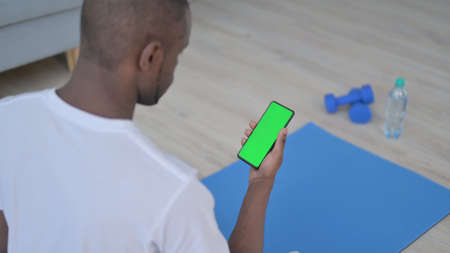 Rear View of African Man using Smartphone with Chroma Key Screen on Yoga Mat