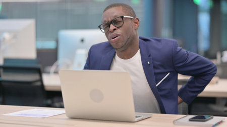 Young African Businessman with Laptop having Back Painの写真素材