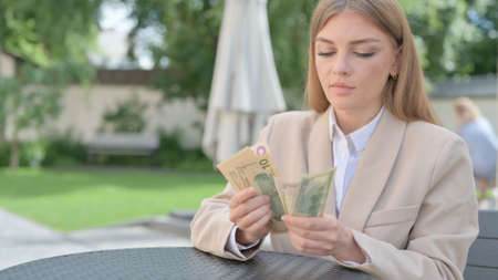 Businesswoman Counting Dollars in Outdoor Cafe