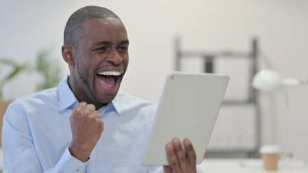 African Man Celebrating Online Success on Tabletの写真素材