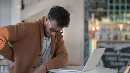 African Man having Back Pain while using Laptop in Cafe