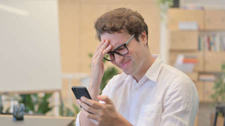 Portrait of Young Man having Loss while Using Smartphone