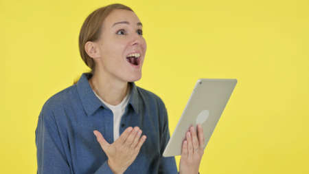 Young Woman Celebrating Success on Tablet on Yellow Backgroundの写真素材