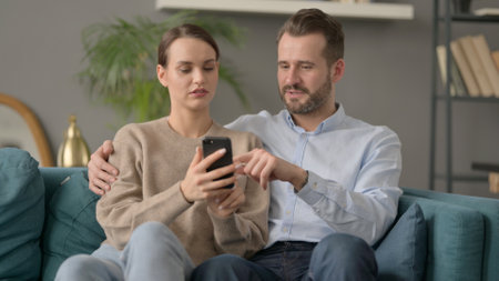 Portrait of Couple using Smartphone While Sitting on Sofaの写真素材