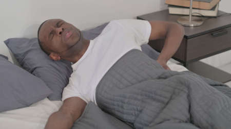African Man having Back Pain while Sleeping in Bed