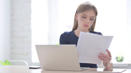 Woman with Laptop Reading Documents in Officeの写真素材