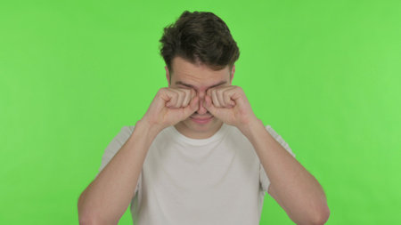 Tired Young Man Rubbing Eyes on Green Backgroundの写真素材