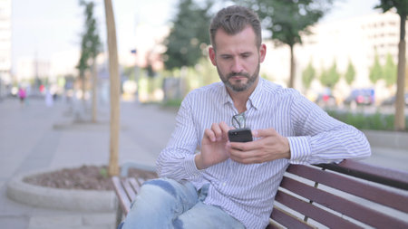 Young Adult Man Using Smartphone while Relaxing on Benchの写真素材