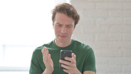 Shocked Casual Young Man Reacting to Loss on Smartphoneの写真素材
