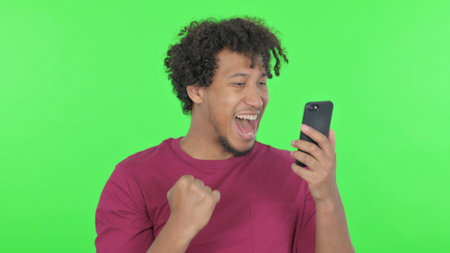 Casual African Man Celebrating on Smartphone on Green Background