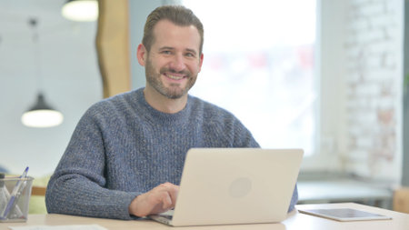 Mature Adult Man Smiling at Camera while using Laptop