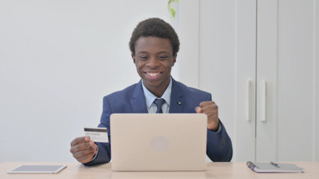 Young African Businessman Enjoying Successful Online Payment on Laptopの写真素材
