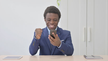 Successful Young African Businessman Celebrating Win on Smartphoneの写真素材