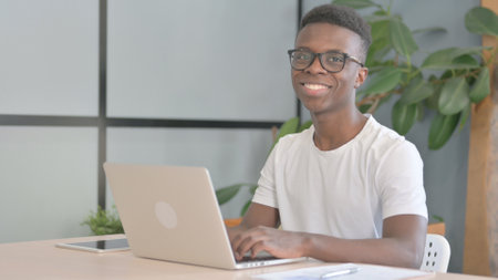 Young African Man Smiling at Camera while using Laptopの写真素材