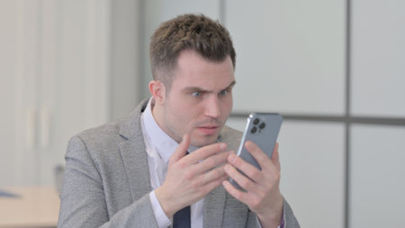 Portrait of Young Businessman Reacting to Loss on Smartphoneの写真素材