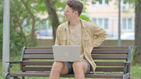 Casual Young Man Using Laptop with Back Pain while Sitting Outdoorの写真素材