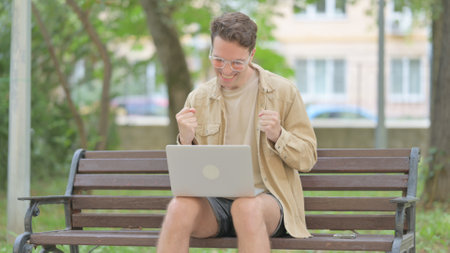 Excited Casual Young Man Celebrating Success on Laptop Outdoorの写真素材