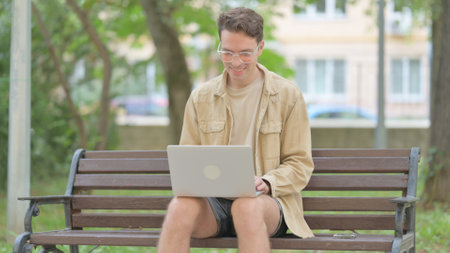 Online Video Chat by Young Man on Laptop Outdoorの写真素材