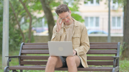 Casual Young Man with Headache Working on Laptop Outdoorの写真素材