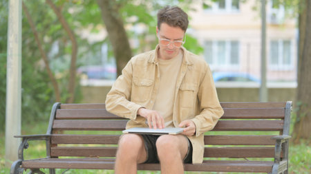 Modern Young Man Sitting and Opening Laptop Outdoorの写真素材