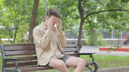 Young Man with Headache Sitting on Benchの写真素材