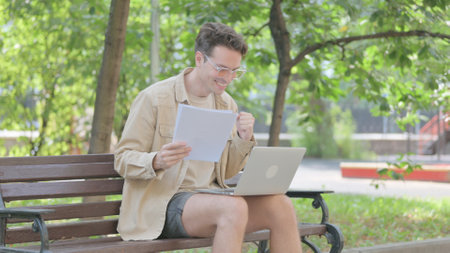 Modern Young Man Celebrating Contract while Working on Laptop Outdoorの写真素材