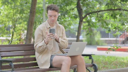Modern Young Man Using Laptop and Phone Outdoorの写真素材