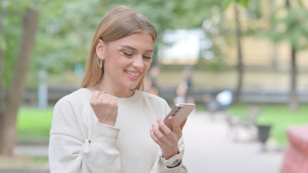 Woman Celebrating Win on Smartphone Outdoorの写真素材