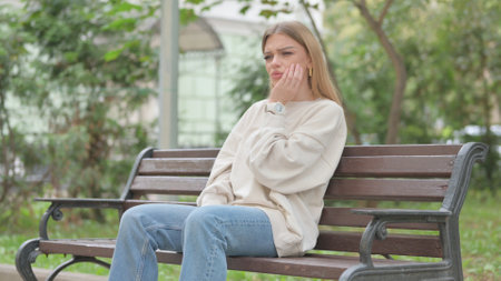 Casual Young Woman with Toothache Sitting Outdoorの写真素材
