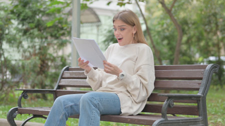 Casual Young Woman Celebrating and Reading Documents Outdoorの写真素材