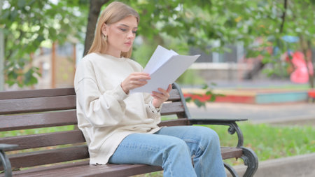 Young Woman Reading Documents while Sitting Outdoorの写真素材