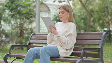 Casual Young Woman using Tablet while Sitting Outdoor on a Benchの写真素材