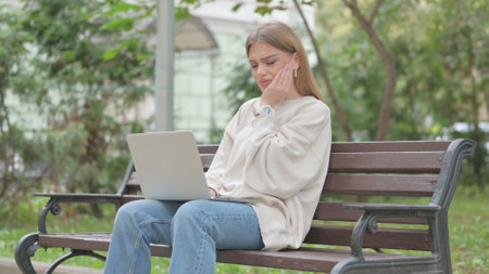 Casual Young Woman with Toothache Working on Laptop Outdoorの写真素材