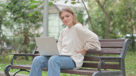Casual Young Woman Using Laptop with Back Pain while Sitting Outdoorの写真素材