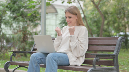 Excited Casual Young Woman Celebrating Success on Laptop Outdoorの写真素材