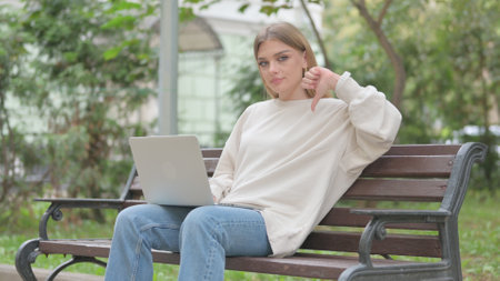 Thumbs Down by Casual Young Woman on Laptop Outdoorの写真素材
