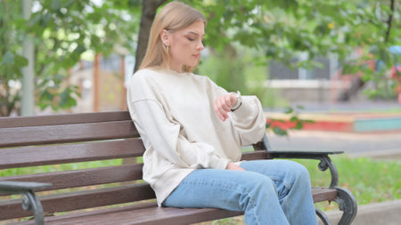 Waiting Young Woman Checking Time on Wrist while Sitting Outdoorの写真素材
