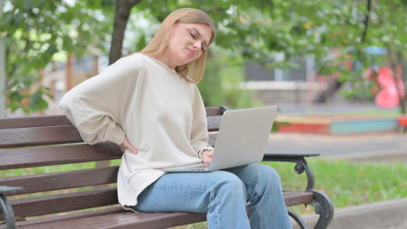 Young Woman Using Laptop with Back Pain while Sitting Outdoorの写真素材