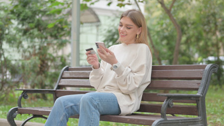 Casual Young Woman Shopping Online while Sitting Outdoorの写真素材