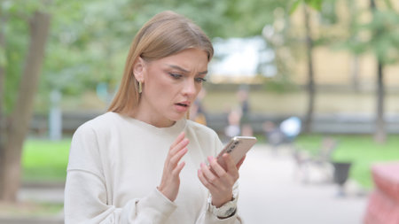 Upset Young Woman get Shocked on Smartphone Outdoorの写真素材