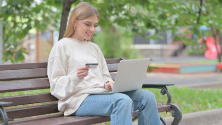 Young Woman Excited for Successful Online Shopping on Laptop Outdoorの写真素材