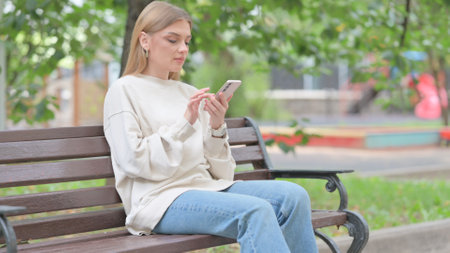 Young Woman using Phone while Sitting Outdoorの写真素材