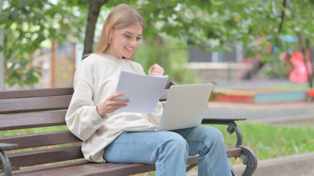Young Woman Celebrating while Using Laptop and Documents Outdoorの写真素材