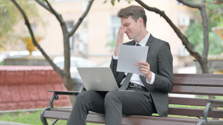 Businessman Feeling Upset while Reading Contract and Using Laptop Outdoorの写真素材