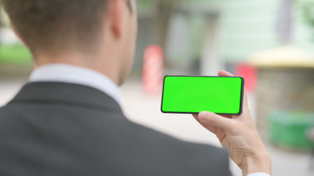 Businessman Horizontally Holding Smartphone with Green Screen Outdoorの写真素材