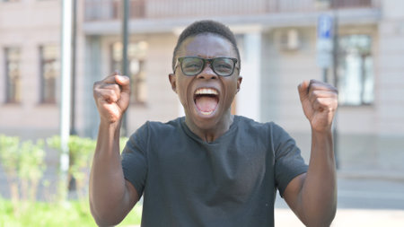 Outdoor Portrait of Excited Young African Man Celebrating Successの写真素材