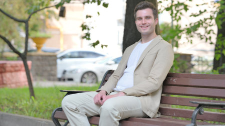 Casual Young Man Smiling at Camera while Sitting Outdoorの写真素材