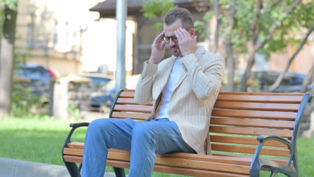 Tired Middle Aged Man Sitting Outdoor with Headacheの写真素材