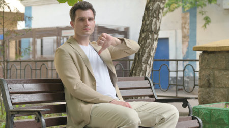 Thumbs Down by Young Man while Sitting Outdoorの写真素材