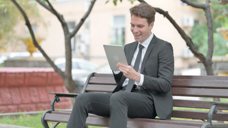Businessman Celebrating on Tablet while Sitting on Benchの写真素材